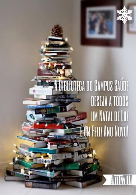 Pilha de livros em forma de pinheiro decorada com iluminação natalina. Terxto: A Biblioteca do Campus Saúde deseja a todos um Natal de Luz e um Feliz Ano Novo!