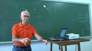Professor acena durante aula em frente à lousa, ainda sem nada escrito