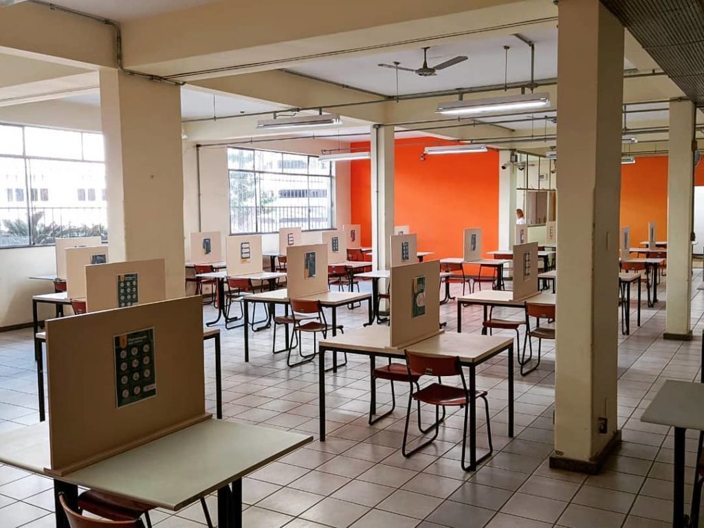 Foto do Restaurante Universitário do campusa Saúde da UFMg. Foto mostra espaço com mesas com divisória no meio.